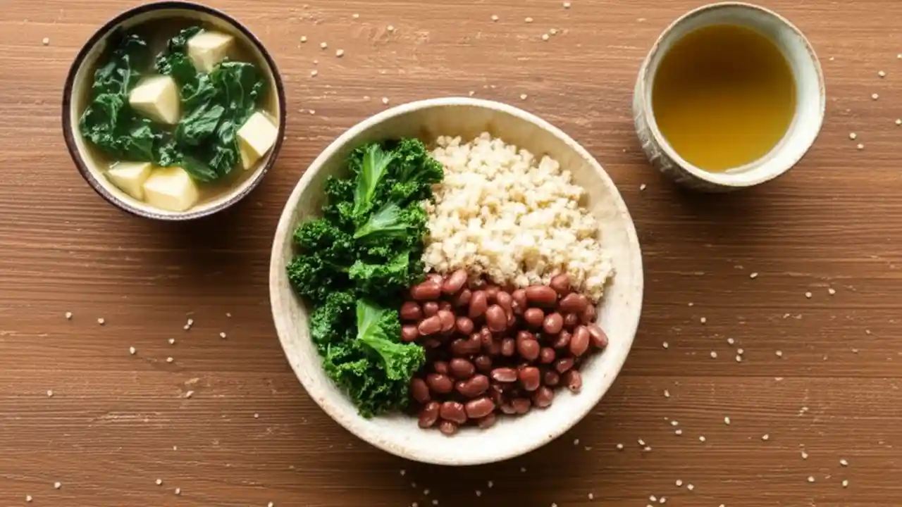 A beginner-friendly macrobiotic meal displayed on a wooden table, featuring a bowl of brown rice, kale, beans, and a side of miso soup.