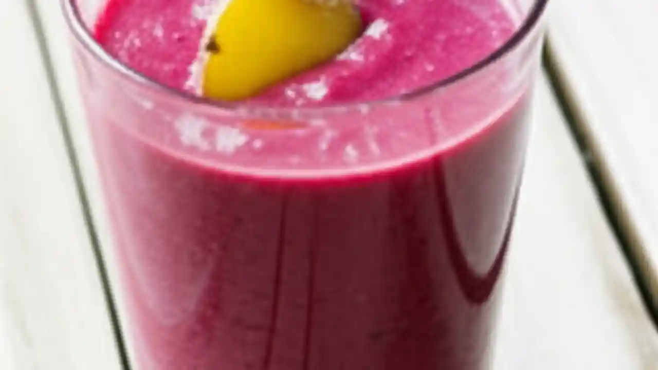 A close-up of a glass of vibrant purple-red Healthy Plum and Ginger Smoothie, garnished with plum and ginger, on a light wooden table.