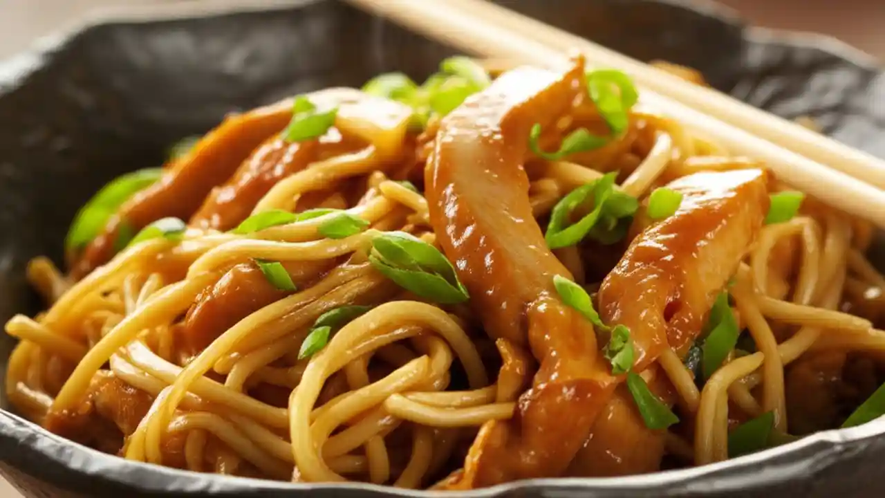 A close-up shot of a bowl of quick and easy chicken lo mein, with glossy noodles, chicken, and vegetables, garnished with scallions.