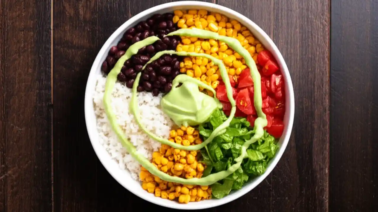 A close-up overhead shot of a healthy vegetarian burrito bowl, filled with cilantro lime rice, black beans, corn salsa, and avocado crema.